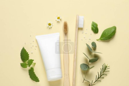 Téléchargez les photos : Composition plate avec brosses à dents en bambou, tube de crème et herbes sur fond beige - en image libre de droit