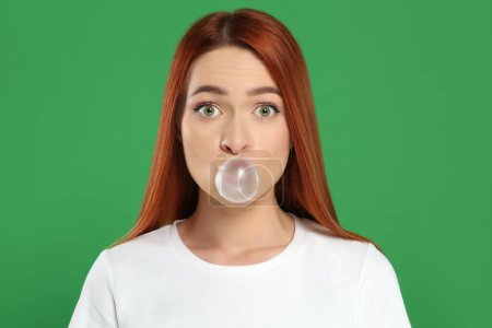 Téléchargez les photos : Femme surprise soufflant de la gomme à bulles sur fond vert - en image libre de droit