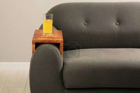 Photo for Glass of juice on sofa with wooden armrest table in room. Interior element - Royalty Free Image