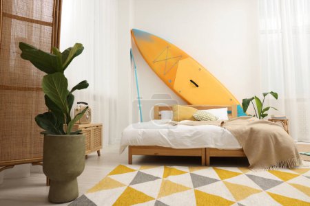 Photo for Large comfortable bed, SUP board and green houseplants in stylish bedroom. Interior design - Royalty Free Image