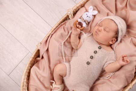 Foto de Lindo bebé recién nacido durmiendo con sonajero en cuna de mimbre en el interior, vista superior. Espacio para texto - Imagen libre de derechos
