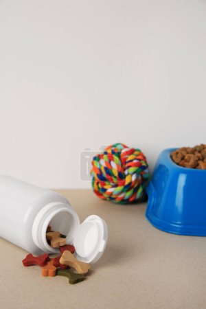 Téléchargez les photos : Bouteille avec vitamines, jouets et aliments secs pour animaux de compagnie dans un bol sur table beige - en image libre de droit