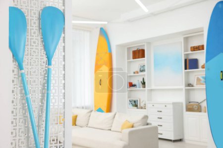 Photo for SUP boards, shelving unit with different decor elements and stylish sofa in room, focus on paddles, space for text. Interior design - Royalty Free Image
