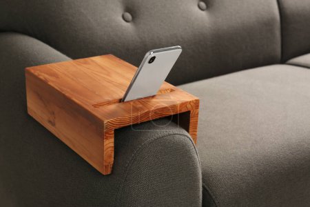 Photo for Smartphone on sofa with wooden armrest table in room, space for text. Interior element - Royalty Free Image
