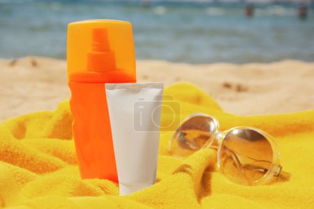 Téléchargez les photos : Écran solaire, lunettes de soleil et serviette sur une plage de sable fin. Soins de protection solaire - en image libre de droit