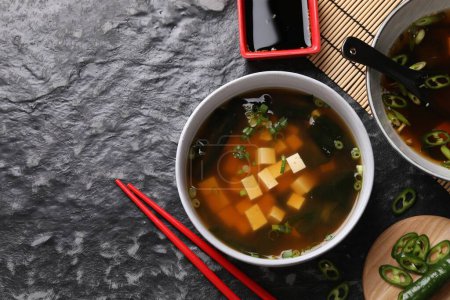 Delicious miso soup with tofu served on black textured table, flat lay. Space for text