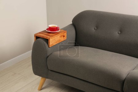 Photo for Cup of tea on sofa with wooden armrest table in room. Interior element - Royalty Free Image