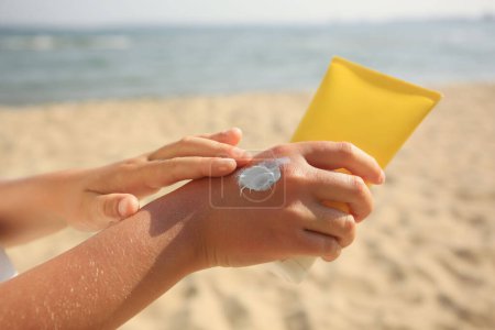Téléchargez les photos : Enfant appliquant de la crème solaire près de la mer, gros plan. Soins de protection solaire - en image libre de droit