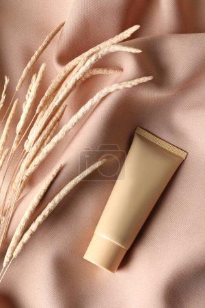 Photo for Tube of skin foundation and decorative plants on beige fabric, flat lay. Makeup product - Royalty Free Image