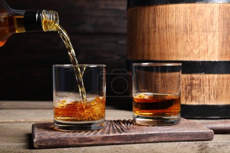 Photo for Pouring whiskey into glass from bottle near wooden barrel on table - Royalty Free Image