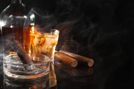 Téléchargez les photos : Cigare, cendrier et whisky fondus sur une surface miroir noire. Espace pour le texte - en image libre de droit