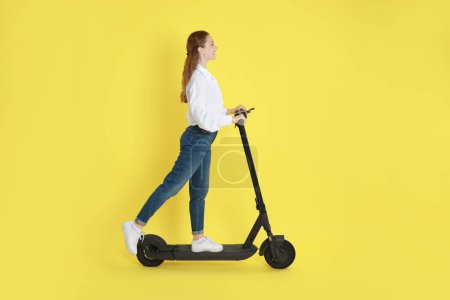 Photo for Happy woman riding modern electric kick scooter on yellow background - Royalty Free Image