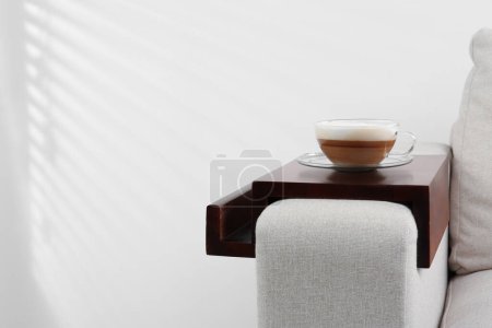 Photo for Cup of coffee on sofa with wooden armrest table indoors, space for text. Interior element - Royalty Free Image