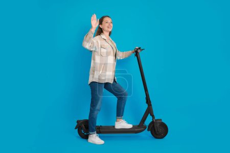 Photo for Happy woman with modern electric kick scooter on light blue background - Royalty Free Image
