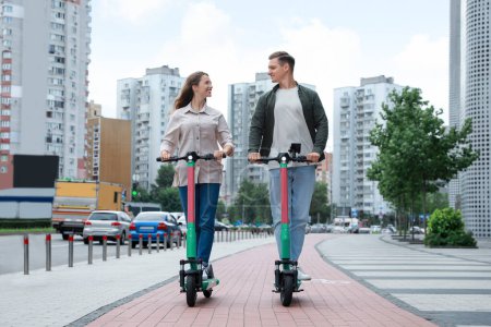 Photo for Happy couple riding modern electric kick scooters on city street - Royalty Free Image