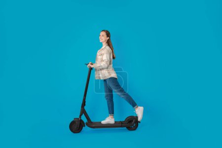 Photo for Happy woman riding modern electric kick scooter on light blue background - Royalty Free Image