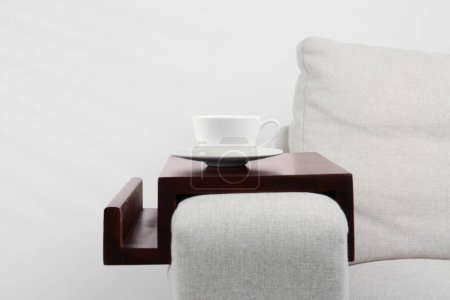 Photo for Cup of coffee on sofa with wooden armrest table indoors. Interior element - Royalty Free Image
