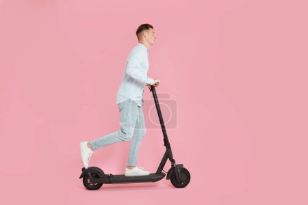 Photo for Young man riding modern electric kick scooter on pink background - Royalty Free Image