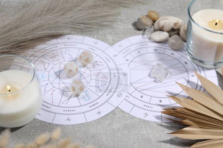 Zodiac wheel, natal chart, burning candles, astrology dices and stones on grey table