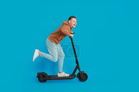 Photo for Emotional man riding modern electric kick scooter on light blue background - Royalty Free Image