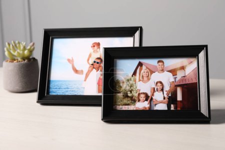 Marcos con fotos familiares y planta de interior sobre mesa de madera blanca