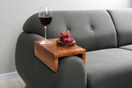 Photo for Glass of red wine and grapes on sofa with wooden armrest table in room. Interior element - Royalty Free Image