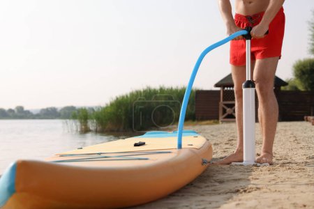Photo for Man pumping up SUP board on river shore, closeup - Royalty Free Image
