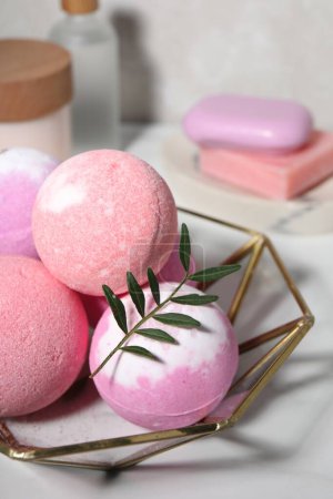 Beautiful aromatic bath bombs and green twig on white table, closeup