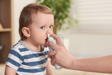 Madre ayudando a su bebé a usar aerosol nasal en interiores