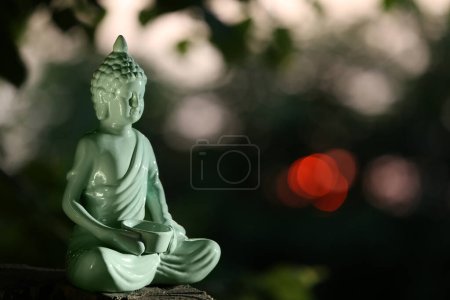 Foto de Estatua decorativa de Buda en el tocón al aire libre por la noche, espacio para el texto - Imagen libre de derechos