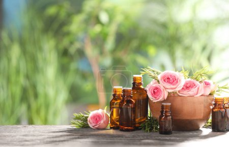 Photo for Bottles with essential oils, roses and rosemary on wooden table against blurred green background. Space for text - Royalty Free Image