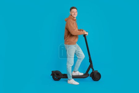 Photo for Happy man with modern electric kick scooter on light blue background - Royalty Free Image