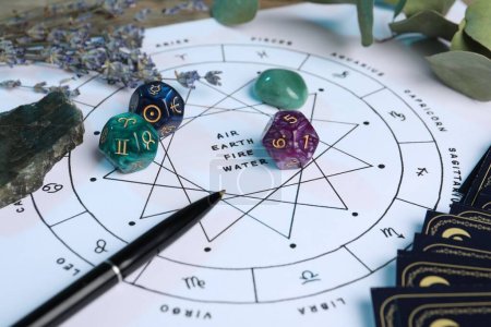 Tierkreisrad mit Zeichen-Dreifaltigkeiten, Kugelschreiber, Edelsteinen und Astrologiewürfeln auf Tisch, Nahaufnahme