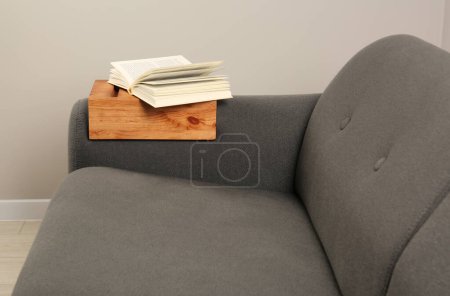 Photo for Open book on sofa with wooden armrest table in room. Interior element - Royalty Free Image