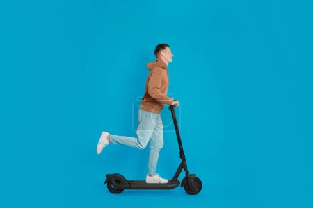 Photo for Young man riding modern electric kick scooter on light blue background - Royalty Free Image