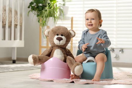 Little child and teddy bear sitting on plastic baby potties indoors