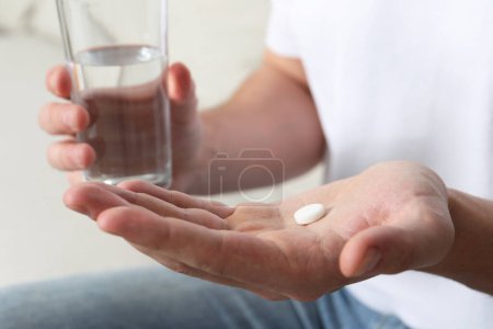 Man with glass of water and pill, closeup view