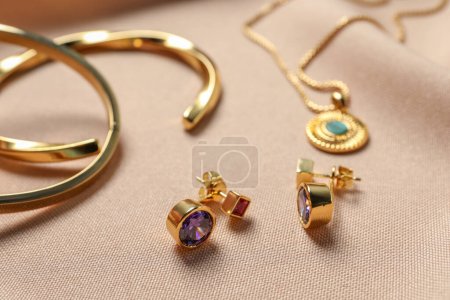 Boucles d'oreilles élégantes, bracelets et collier sur tissu beige, gros plan