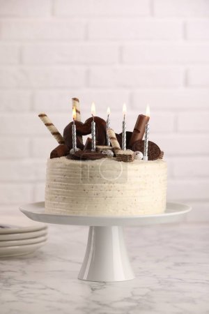 Téléchargez les photos : Délicieux gâteau décoré de bonbons et de bougies allumées sur une table en marbre blanc - en image libre de droit