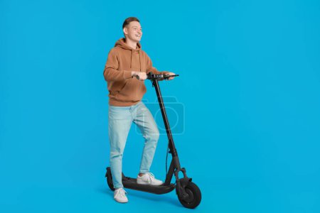 Photo for Happy man with modern electric kick scooter on light blue background - Royalty Free Image