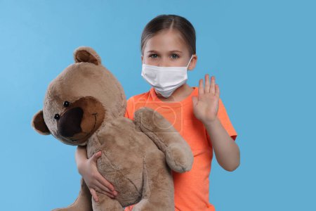 Téléchargez les photos : Jolie fille avec masque médical et ours en peluche sur fond bleu clair - en image libre de droit