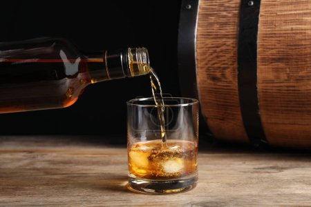 Téléchargez les photos : Verser le whisky de la bouteille dans du verre sur une table en bois - en image libre de droit