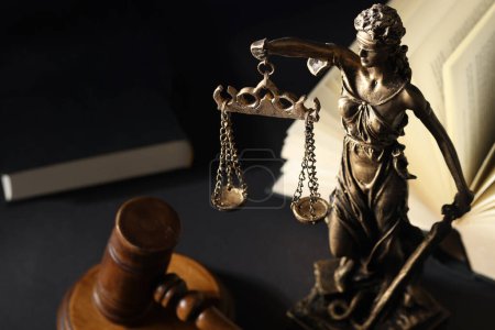 Símbolo de trato justo bajo la ley. Estatua de Lady Justice cerca del mazo y libro abierto sobre mesa negra