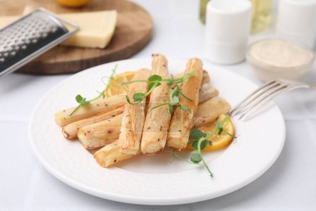 Plate with baked salsify roots and lemon on white table, closeup