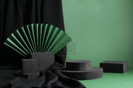 Schwarze geometrische Figuren und Papierfächer auf grünem Hintergrund. Stilvolle Präsentation für Produkt