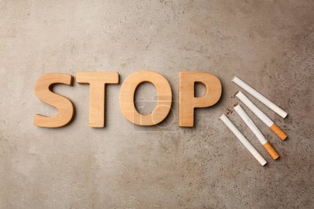 Téléchargez les photos : Mot Stop en lettres de bois et cigarettes sur table texturée grise, pose plate. Concept non fumeur - en image libre de droit