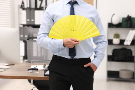 Foto de Empresario con abanico de mano amarillo en oficina, primer plano - Imagen libre de derechos