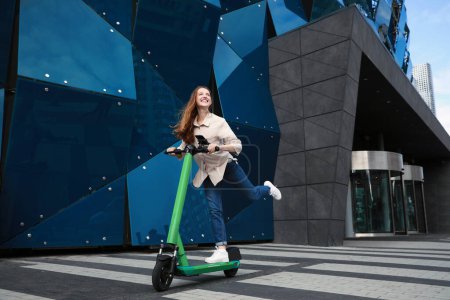 Photo for Happy woman riding modern electric kick scooter on city street - Royalty Free Image