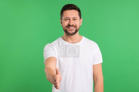 Téléchargez les photos : Homme heureux accueillant et offrant poignée de main sur fond vert - en image libre de droit