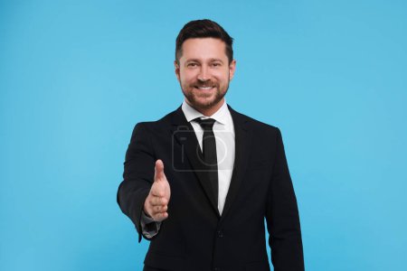 Téléchargez les photos : Homme heureux accueillant et offrant poignée de main sur fond bleu clair - en image libre de droit